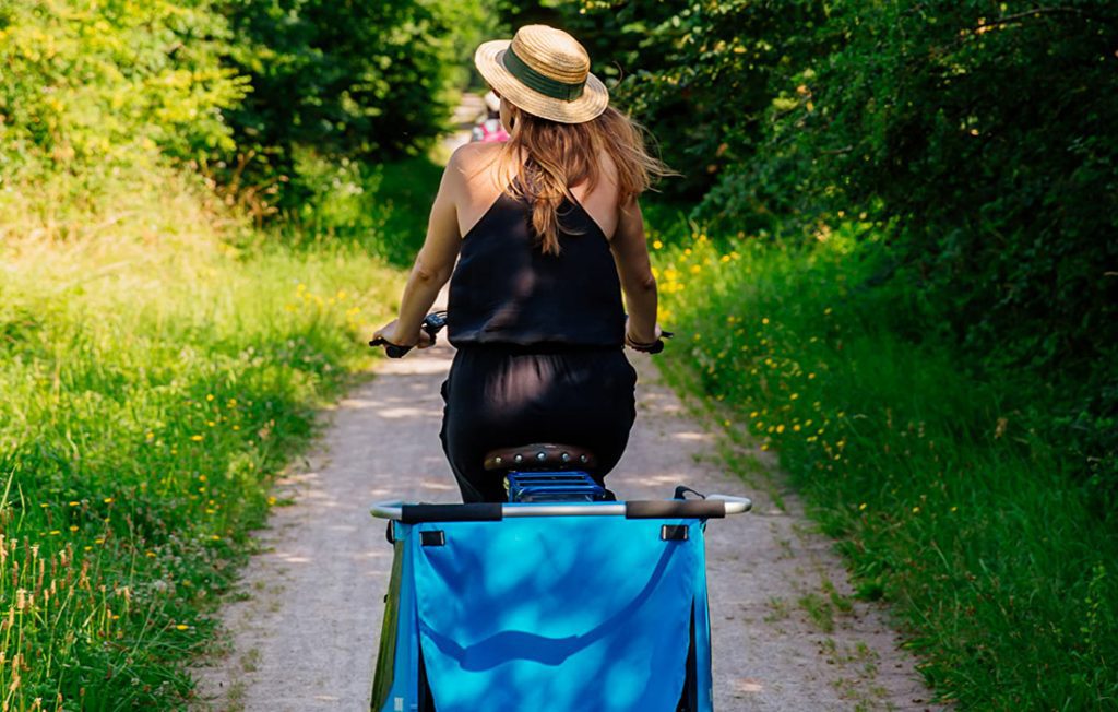 Femme portant un chapeau en balade en vélo sur un petit chemin de forêt